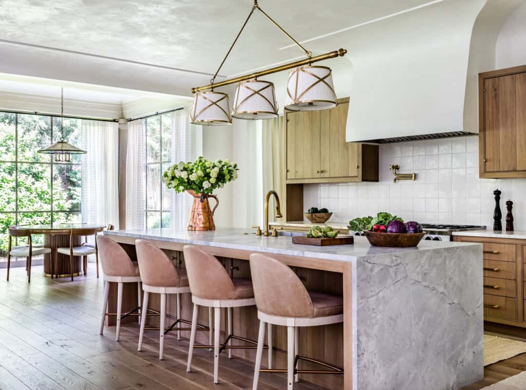 Modern kitchen with marble island, pink bar stools, and natural light.