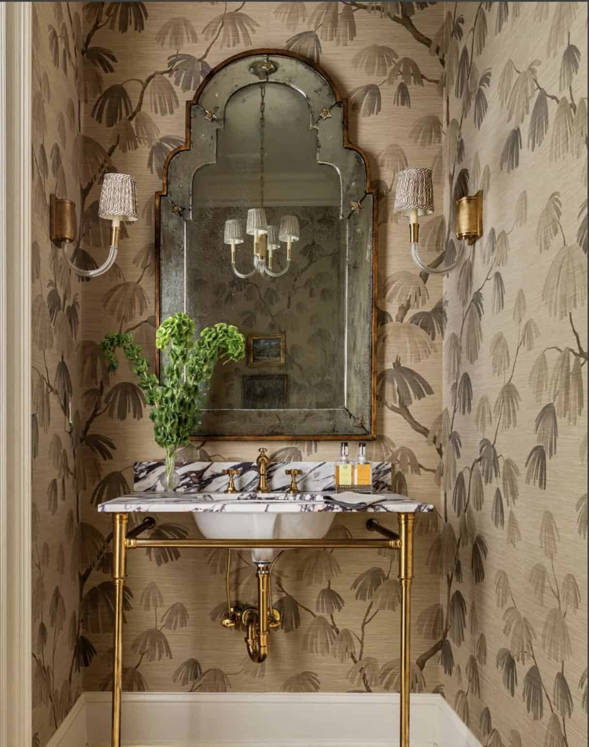 Elegant vintage bathroom with gold fixtures, patterned wallpaper, and a decorative mirror above a ma.